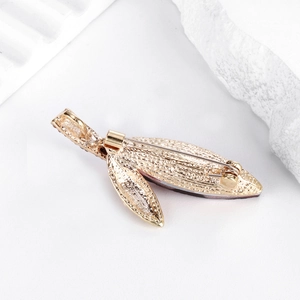 Elegant gold leaf brooch with full rhinestone inlay on white stone pedestal