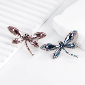 Squisite spille a libellula con gemme rosa e blu su un espositore bianco minimalista