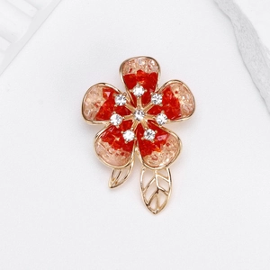 Elegant camellia brooch with red crystal petals and gold metal leaves on white background