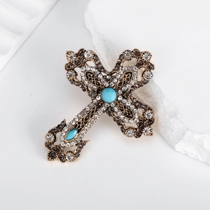 Spilla a croce vintage con strass e pietre turchesi su elegante sfondo di pietra