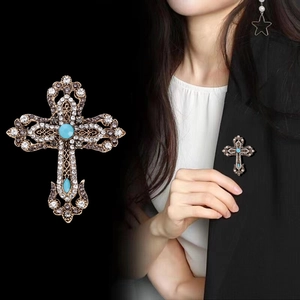 Spilla a croce vintage dorata con turchese e strass su blazer nero per un look barocco