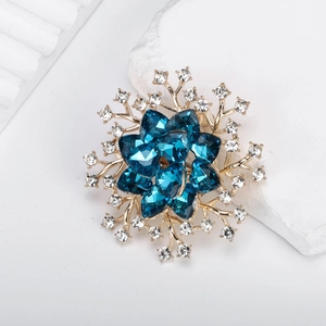 Luxuriöse goldene Blumenbrosche mit blauen Herzkristallen und Strass auf weißem Marmor
