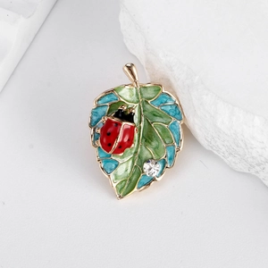 Elegant gold enamel ladybug and leaf brooch with crystal stone on white stone background