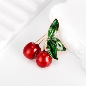 Elegant red cherry brooch with green leaves and gold plating on white stone background