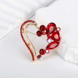 Elegant gold heart brooch with red rhinestones and crystals on a white stone surface