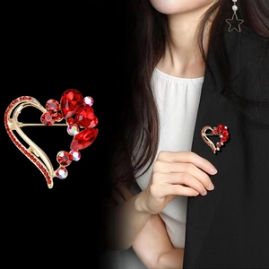 Elegant gold heart brooch with red crystals shown as a close-up and worn on a black blazer
