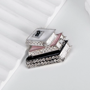Detailed close-up of stacked book-shaped brooches with colorful enamel and sparkling rhinestones