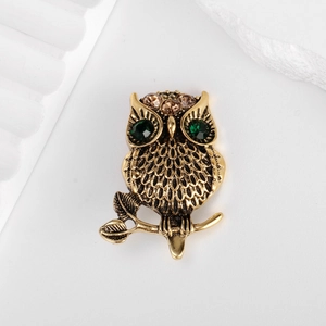 Vintage gold owl brooch with green gemstone eyes perched on a branch, main view