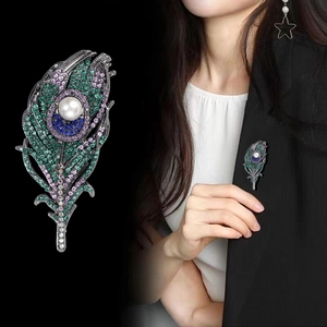 Detail view of a luxury peacock feather brooch with colorful crystals and a white pearl