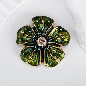 Broche fleur vintage avec émail vert et cristaux bleus sur un fond décoratif gris