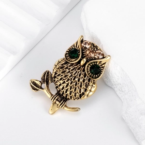 Vintage owl brooch in antique gold with deep green crystal eyes on a white stone
