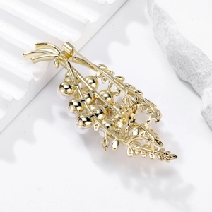 Broche élégante en perles dorées pour femme présentée sur un fond blanc texturé