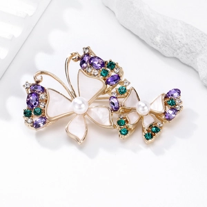 Elegante spilla a farfalla dorata con perle e cristalli colorati su sfondo di pietra