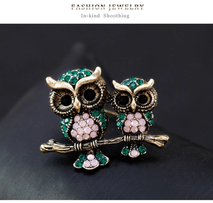 Macro view of vintage owl brooch with green and pink rhinestones on antique gold branch