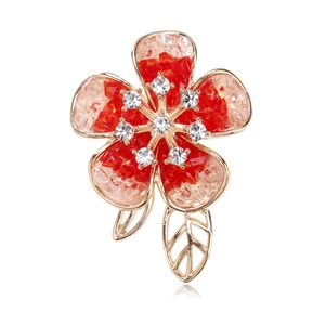 Detail of flower brooch with gradient red crystals and golden leaves on white background