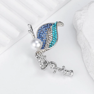Elegant silver leaf brooch with blue rhinestones and a white pearl on white pedestal