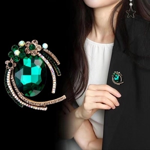 Detailed close-up of emerald green crystal brooch with floral rhinestones and gold plating