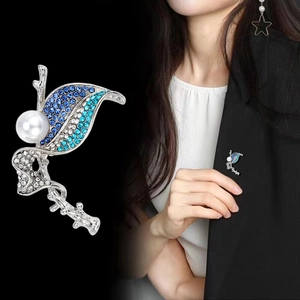 Elegant silver leaf brooch with blue crystals and white pearl worn on a black suit lapel