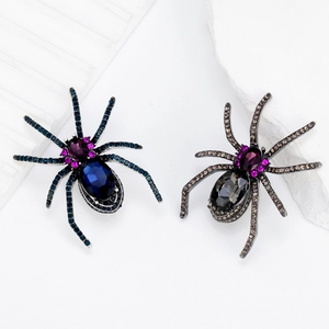Exaggerated spider brooches with blue and grey crystals on white stone surface