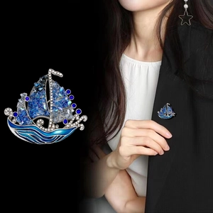 Elegante broche de velero en esmalte azul sobre traje negro, mostrando un estilo de lujo