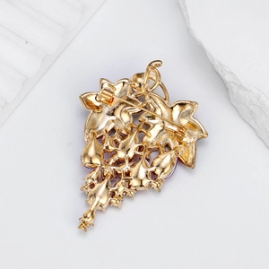 Eleganter Trauben-Anstecker aus Goldlegierung mit Nadelverschluss auf Steinhintergrund