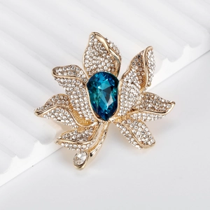 Elegant gold lotus brooch with sparkling white crystals and a blue teardrop gemstone