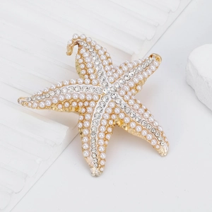 Élégante broche étoile de mer dorée avec perles blanches et strass brillants sur fond blanc