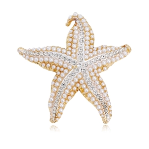 Broche étoile de mer dorée avec perles blanches et strass brillants sur fond blanc