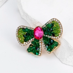 Élégante broche nœud en cristal avec cristaux verts et pierre centrale rose sur métal doré