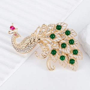 Elegant peacock brooch with green beads and rhinestones on white stone background