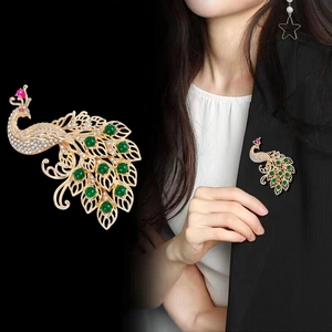 Golden peacock brooch with green beads and white crystals shown on a black suit lapel