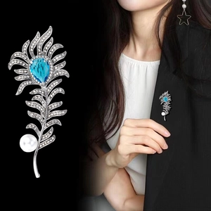 Elegant silver feather brooch with blue gemstone and white pearl shown on black suit