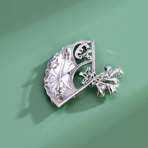 Elegant silver fan-shaped brooch with pearl flower accents on a green background