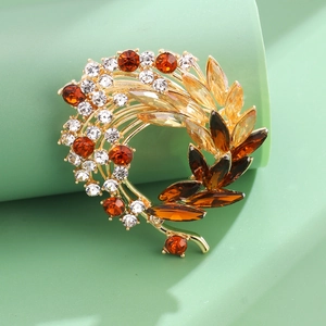 Vintage floral wreath brooch with amber crystals and gold base on a green stand
