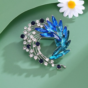 Macro detail of silver brooch with blue crystals and white rhinestones on green background