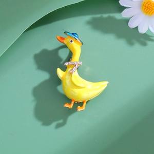 Cute yellow duck enamel brooch with blue hat and crystal tie on a green background