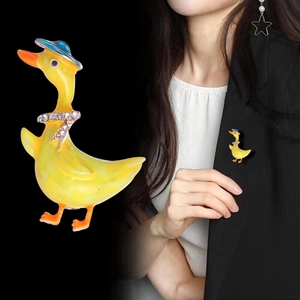 Detailed close-up of a cute yellow duck enamel brooch with a blue hat and diamond scarf