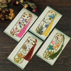 Detail of four hollow metal bookmarks with colorful silk tassels on a dark wood background