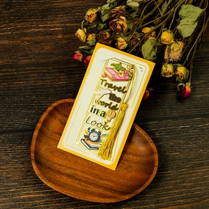 Macro detail of a yellow travel-themed metal bookmark with golden tassel and wood backdrop