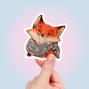 Detail of cartoon fox sticker with gray scarf held by hand for laptop decoration
