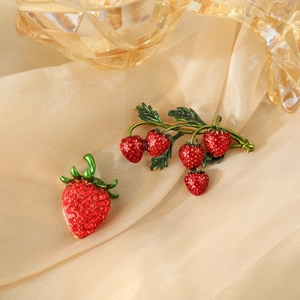 Elegant strawberry brooch set with red rhinestones and gold alloy on silk fabric background