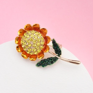Vue macro d'une broche tournesol avec cristaux jaunes et émail orange sur fond doré