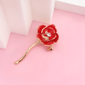 Détail d'une broche rose rouge à bords dorés et centre en zircon sur fond rose