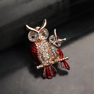 Gros plan d'une broche chouette avec émail rouge et strass blancs étincelants