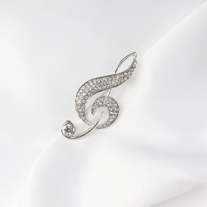 Elegante broche de clave de sol plateado con brillantes pedrería sobre seda blanca