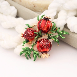 Macro view of pomegranate brooch with red enamel seeds and green leaves on gold plating