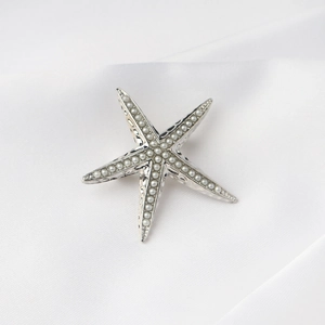 Primer plano de broche de estrella de mar plateado con perlas sobre raso suave