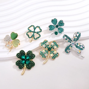 Detail of six clover brooches with emerald crystals and gold alloy plating set on white