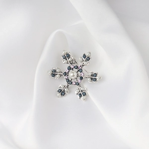 Elegante broche de copo de nieve con cristales azules y perlas sobre seda blanca