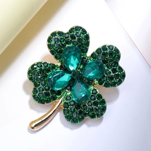 Close-up of golden clover brooch with emerald green teardrop crystals and pave accents